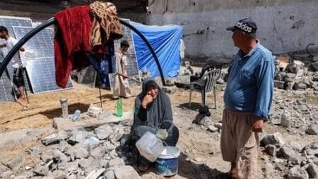 A woman sits at a tent pitched by a destroyed building in Rafah