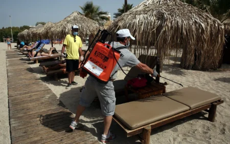 A man wearing a face mask disinfects a sunbed on a beach in Athens (Picture: AFP)